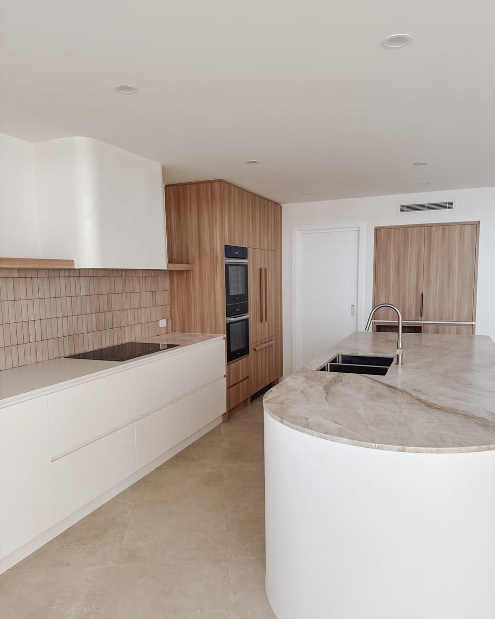 Curved white island with a natural stone top, rendered rangehood and timber tall cabinetry