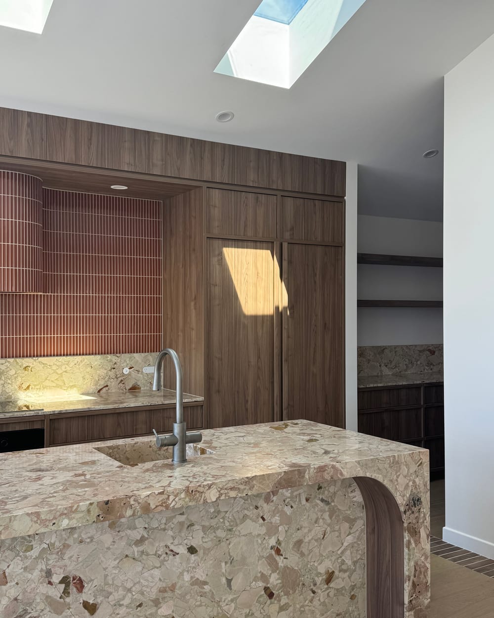 Terrazzo island with a curved timber edge, walnut cabinetry and a terracotta tiled splashback